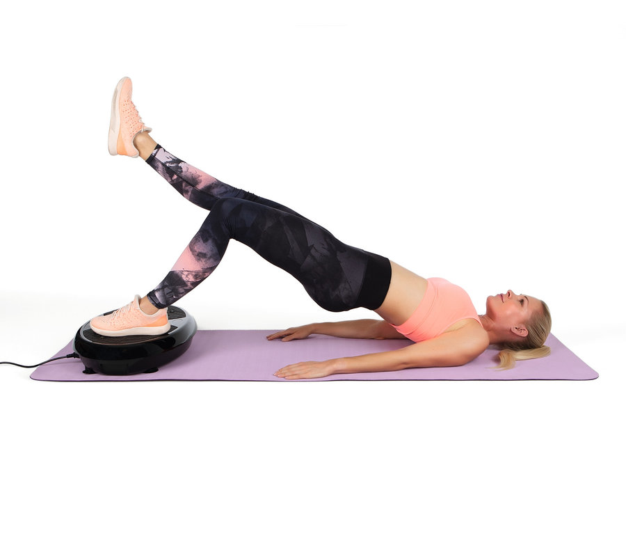 Frau trainiert auf einer lila Matte mit einem Bein auf dem VITALmaxx Vibrationstrainer.