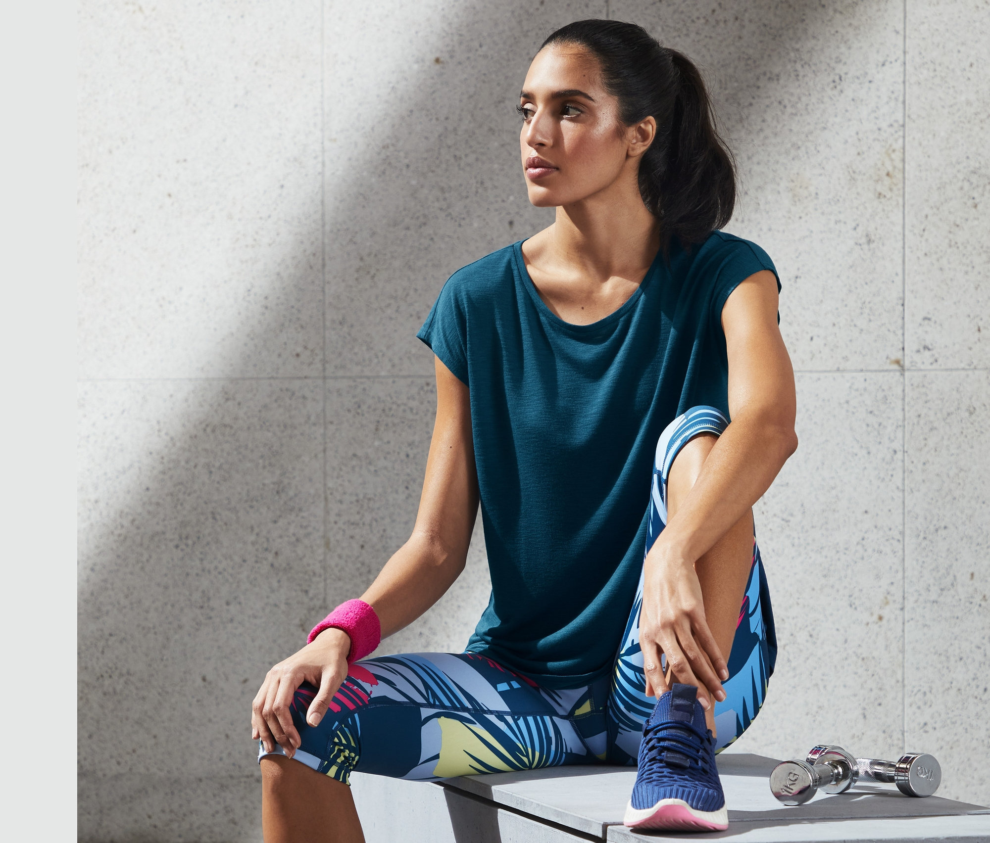 Frau sitzt auf Bank, trägt blaues Sportshirt.
