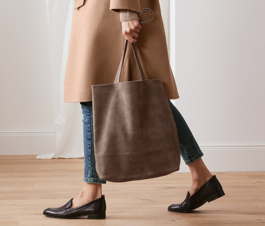 Frau geht und trägt einen Shopper aus chromfrei gegerbtem Veloursleder und trägt einen Wollmantel mit Cashmere.