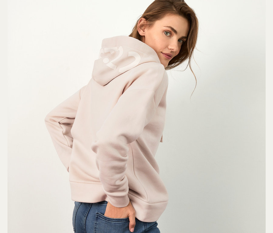 Frau posiert in hellrosa Hoodie und blauen Jeans.
