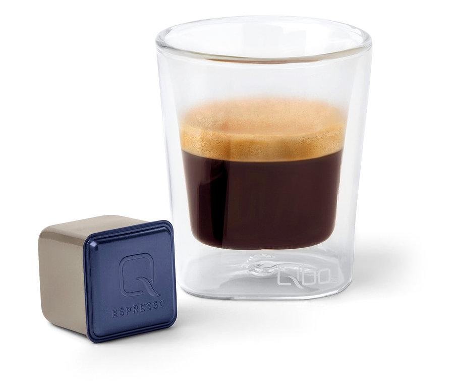 Eine Qbo Espresso INDIAN KAVERI Kapsel neben einem Glas Espresso.