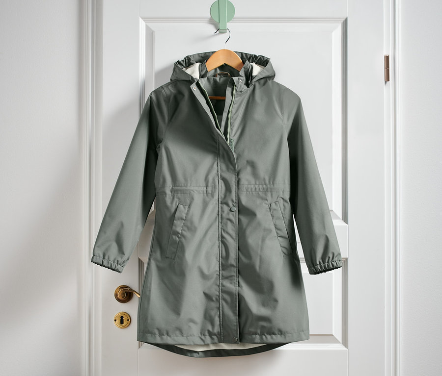 Ein grüner Regenparka hängt an einer weißen Tür.
