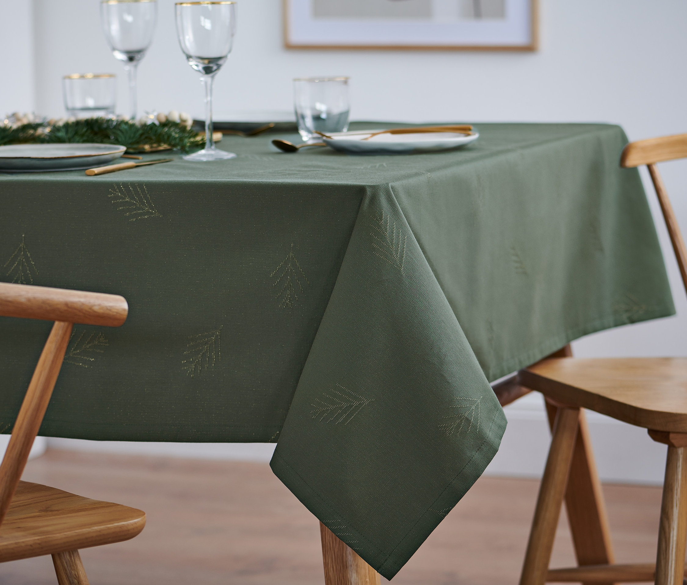 Auf einem Tisch liegt eine grüne Jacquard-Tischdecke in Normalgröße mit Nadelbaum-Motiv, auf der Teller, Gläser und Besteck angeordnet sind.