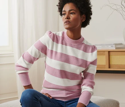 Frau sitzt und trägt einen Pullover mit Puffärmeln und Jeans.