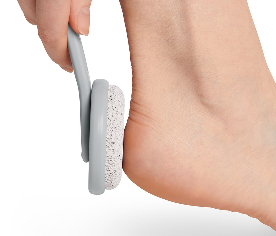 Hand hält Bimsstein aus dem Fußpflege-Set an der Ferse des Fußes.