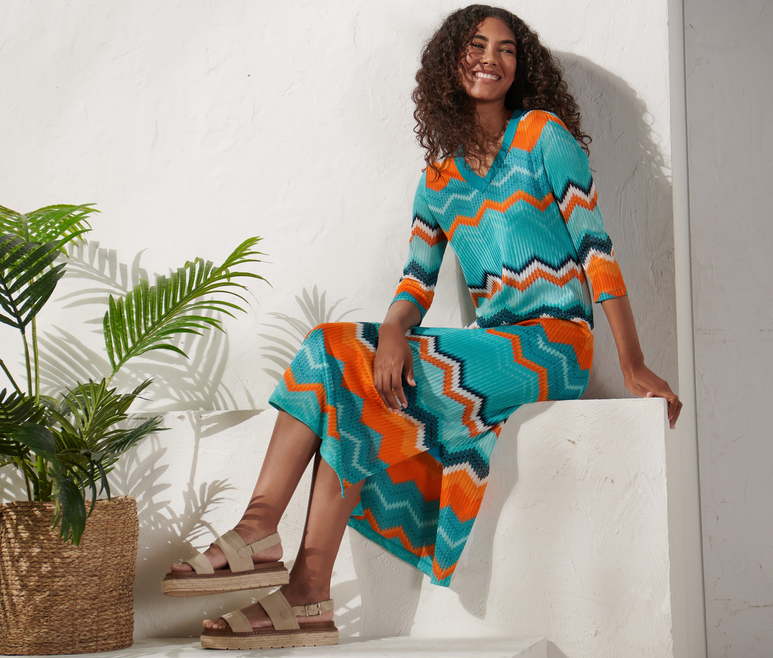 Frau sitzt auf weißem Sockel und trägt ein Strickkleid.