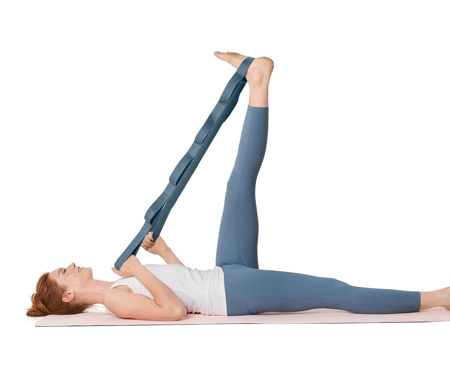 Eine Frau liegt auf einer Matte und dehnt ihr Bein mit einem Stretch-Strap.