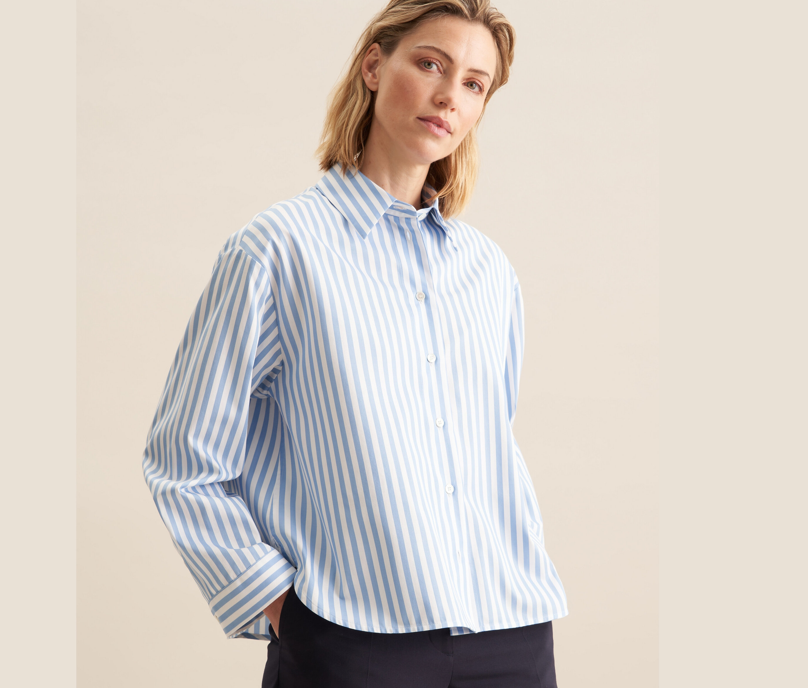 Frau trägt eine blaue, gestreifte Seidensticker Oversize Hemdbluse mit weißen Streifen und eine dunkelblaue Hose.