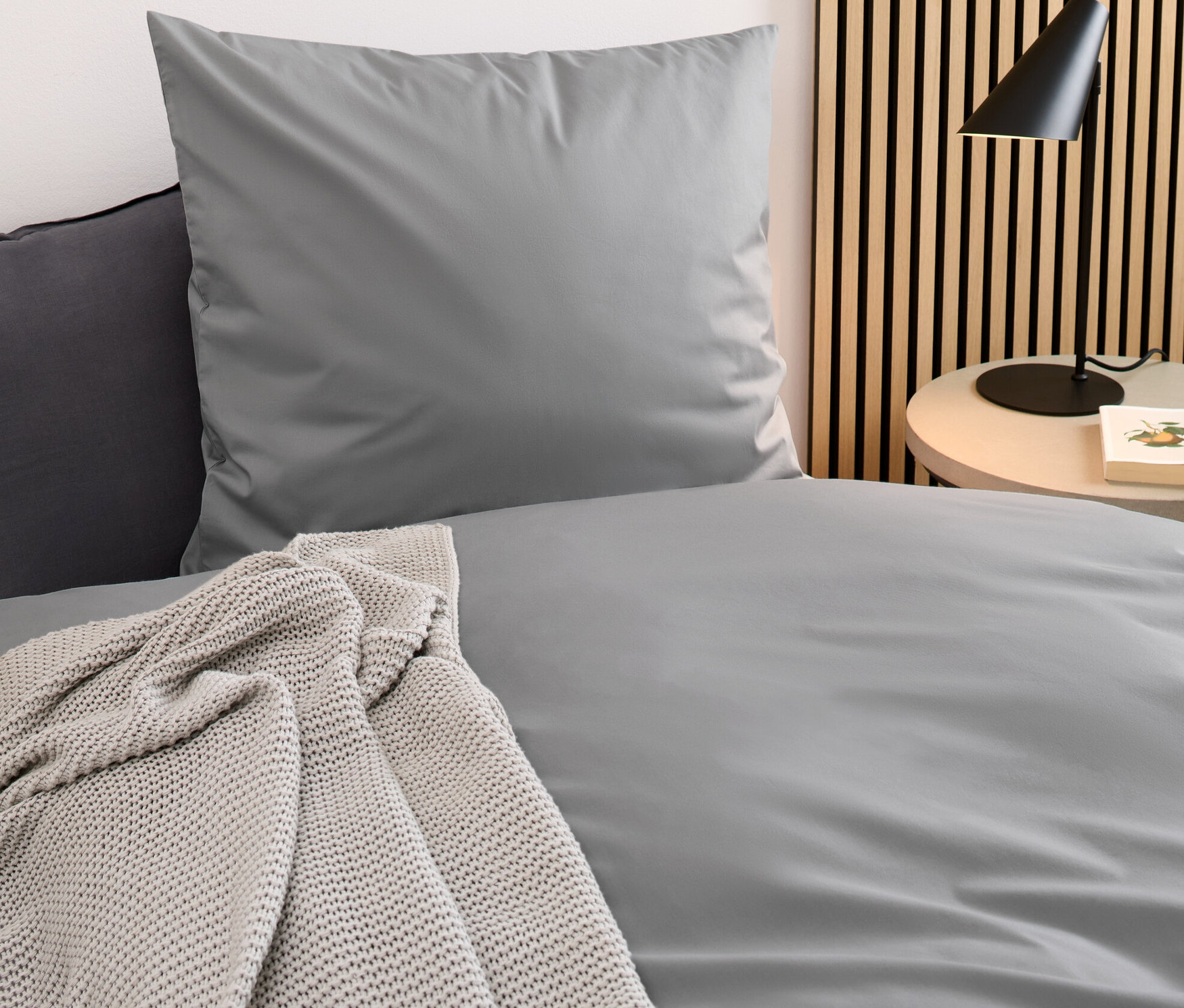 Detail einer grauen Perkal-Bettwäsche in Normalgröße und einer grauen Perkal-Bettwäsche in Übergröße.