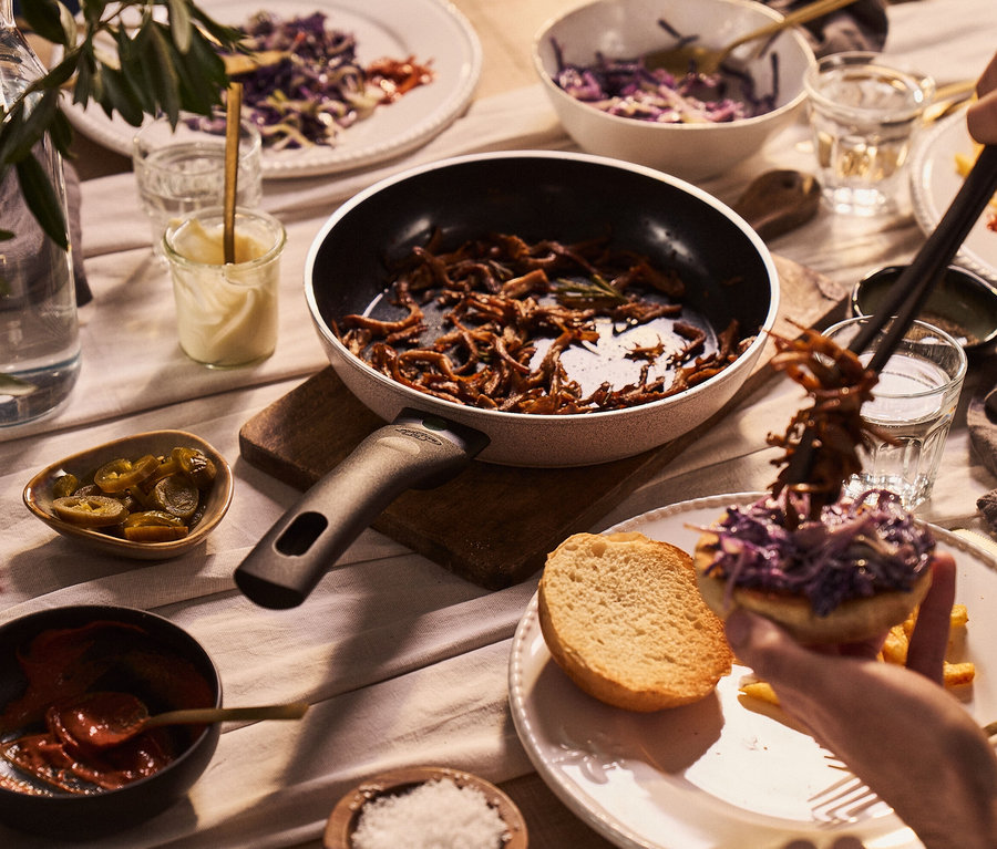 Auf einem Tisch stehen eine Pfanne mit Inhalt, daneben Schüsseln mit Essen und Gläser mit Getränken. Zu sehen ist auch eine BALLARINI Aluminium-Bratpfanne, sand, 20 cm.