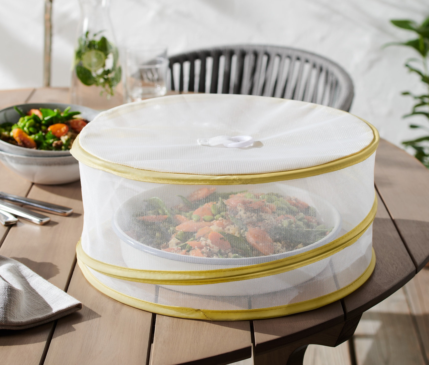 Auf einem Holztisch steht eine Mahlzeit, die mit einer faltbaren Abdeckhaube abgedeckt ist.