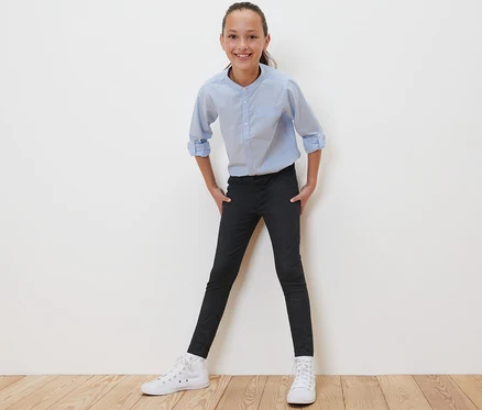 Ein Mädchen posiert in schwarzen Kinder-Treggings – Fit »Jule«, einem hellblauen Hemd und weißen Turnschuhen.