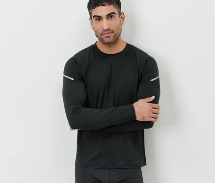 Mann mit verschränkten Armen, der an einer Wand steht und ein schwarzes Langarm-Funktionsshirt trägt.