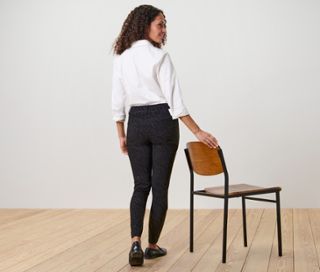 Frau posiert in bedruckter Bengalin-Hose und weißem Hemd neben einem Stuhl.