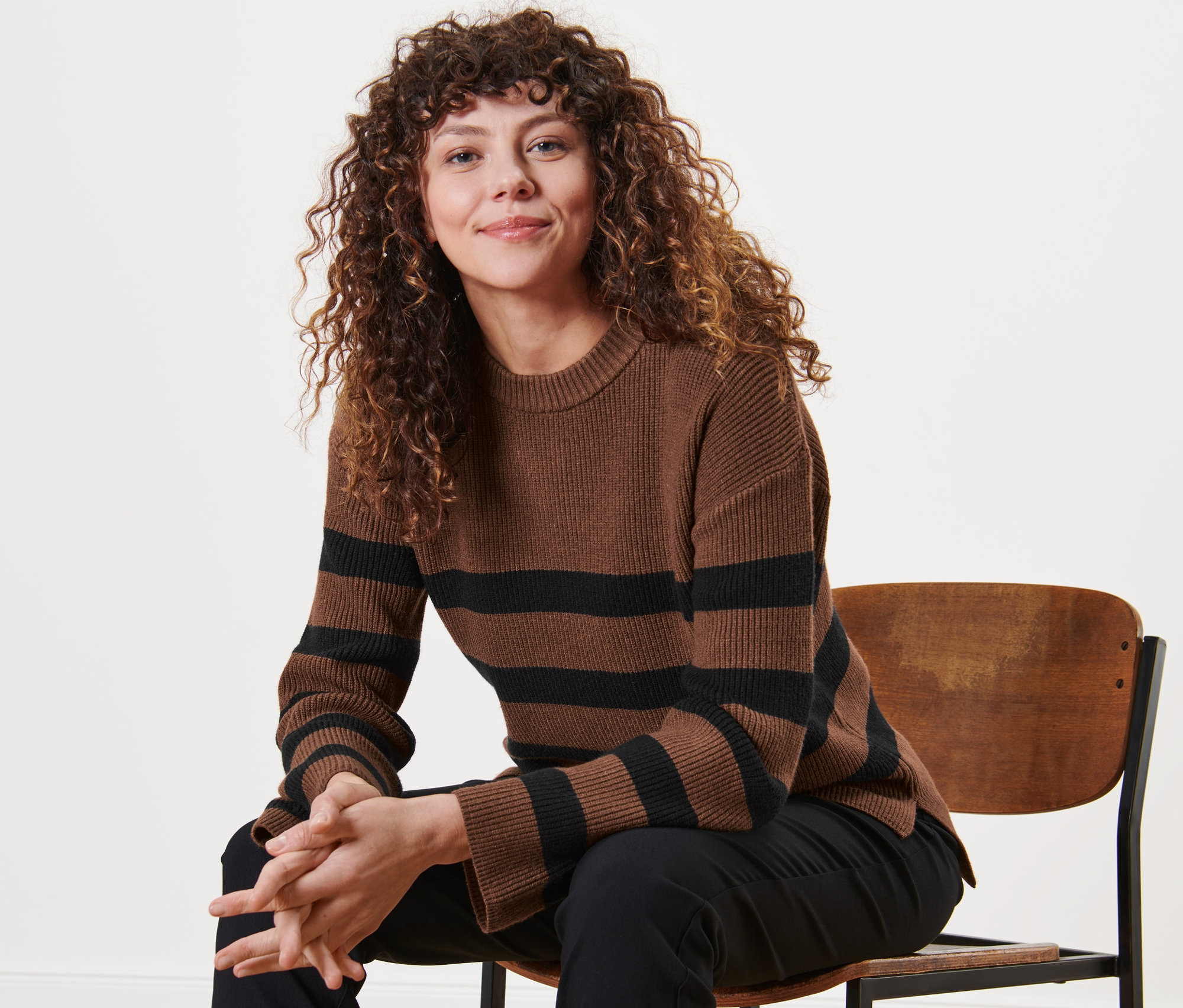 Frau sitzt auf einem Stuhl und trägt einen gestreiften Strickpullover.