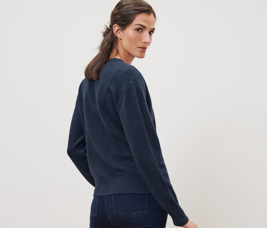 Frau blickt über die Schulter und trägt eine dunkelblaue Strickjacke mit Wolle und Jeans.