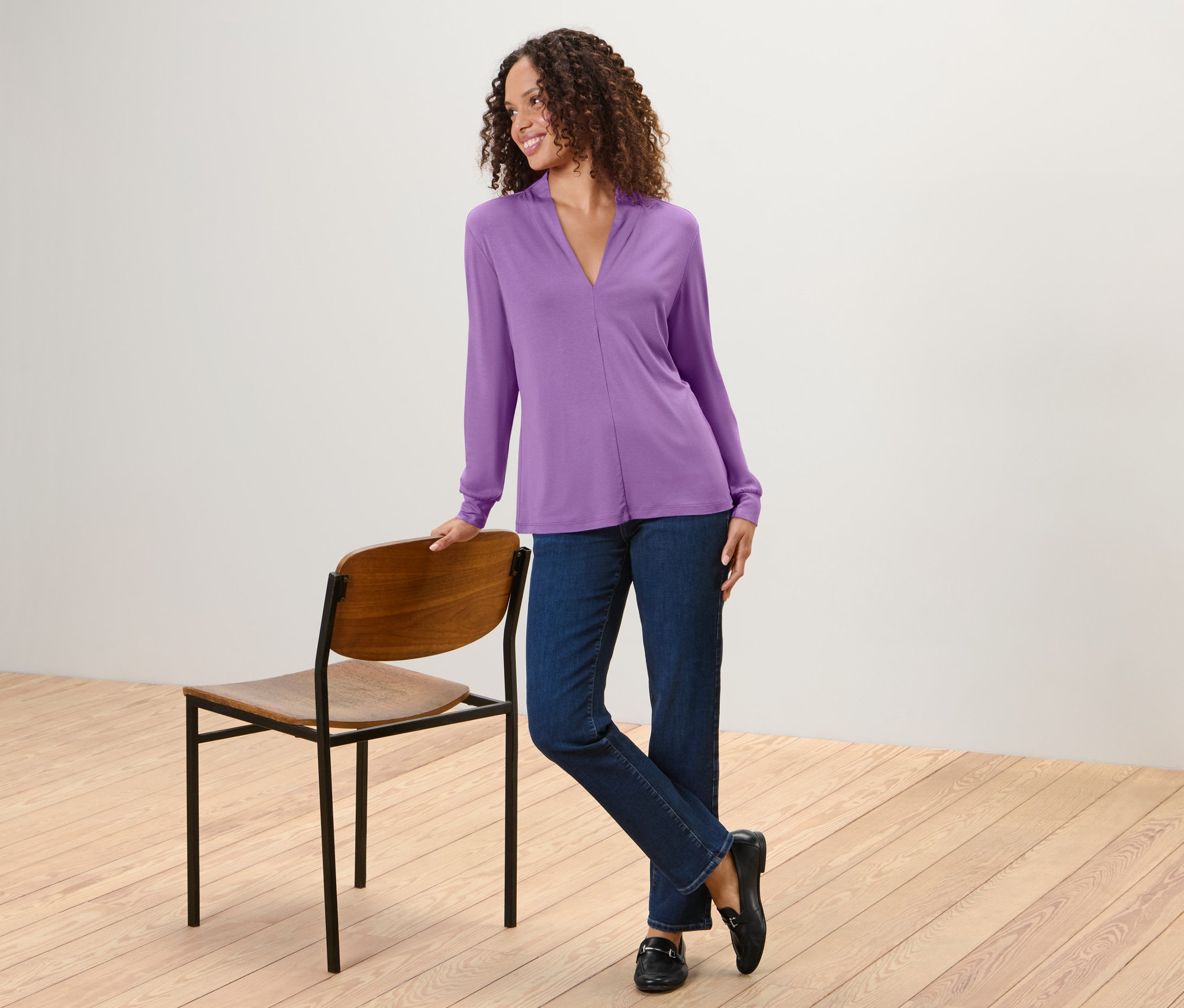 Frau posiert in einem Blusenshirt mit V-Ausschnitt, Jeans und Mokassins.