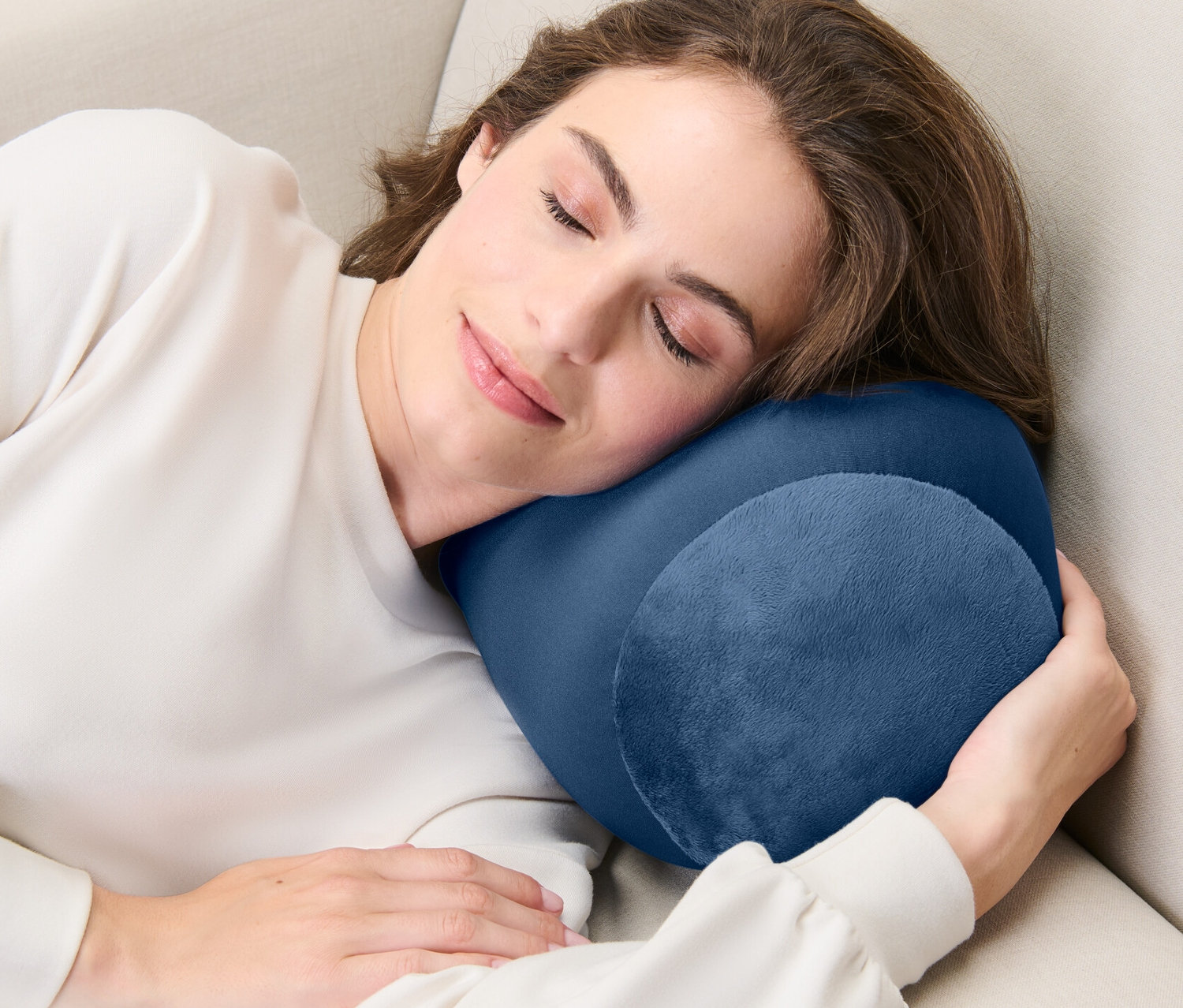 Frau schläft auf einem beigen Sofa mit einem Relaxkissen.