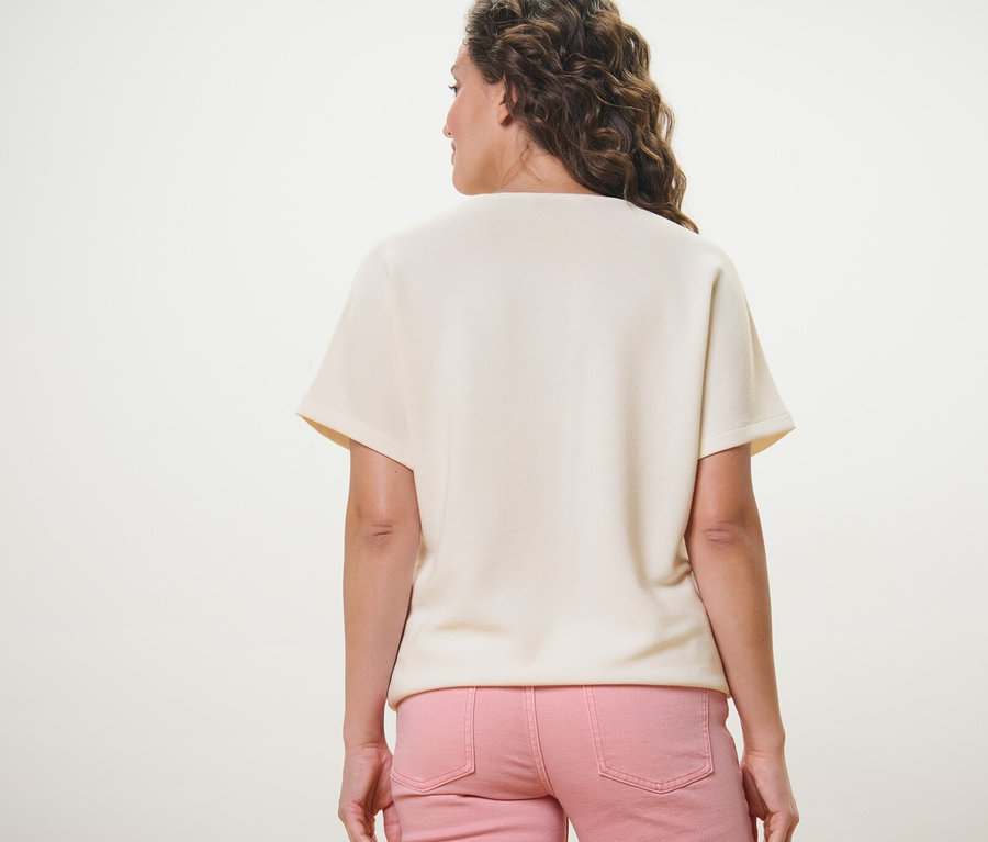 Rückansicht einer Frau in einem cremeweißen Blusenshirt und einer rosafarbenen Hose.