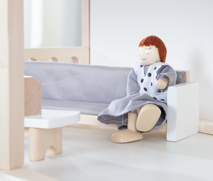 Puppe sitzt auf einem grauen Sofa im roba Puppenhaus inkl. Zubehör.