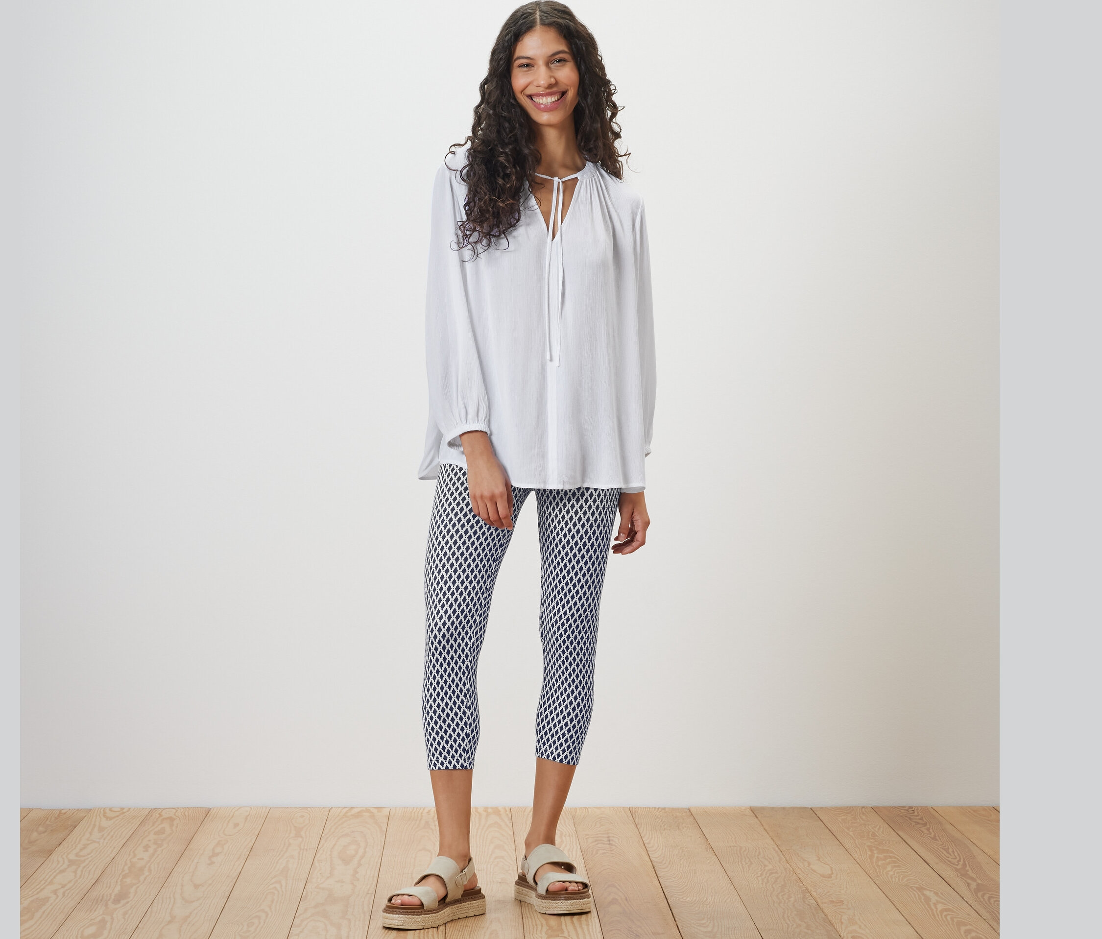 Frau steht und trägt eine weiße Bluse und bedruckte 3/4-Leggings.