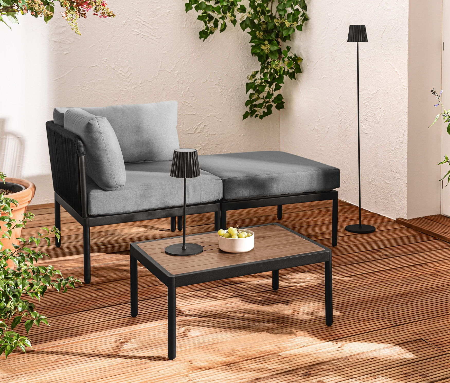 Terrasse mit modularer Lounge mit Textilgeflecht, schwarzer LED-Akku-Outdoor-Tischleuchte und Stehleuchte, sowie LED-Filament-Lichterkette.