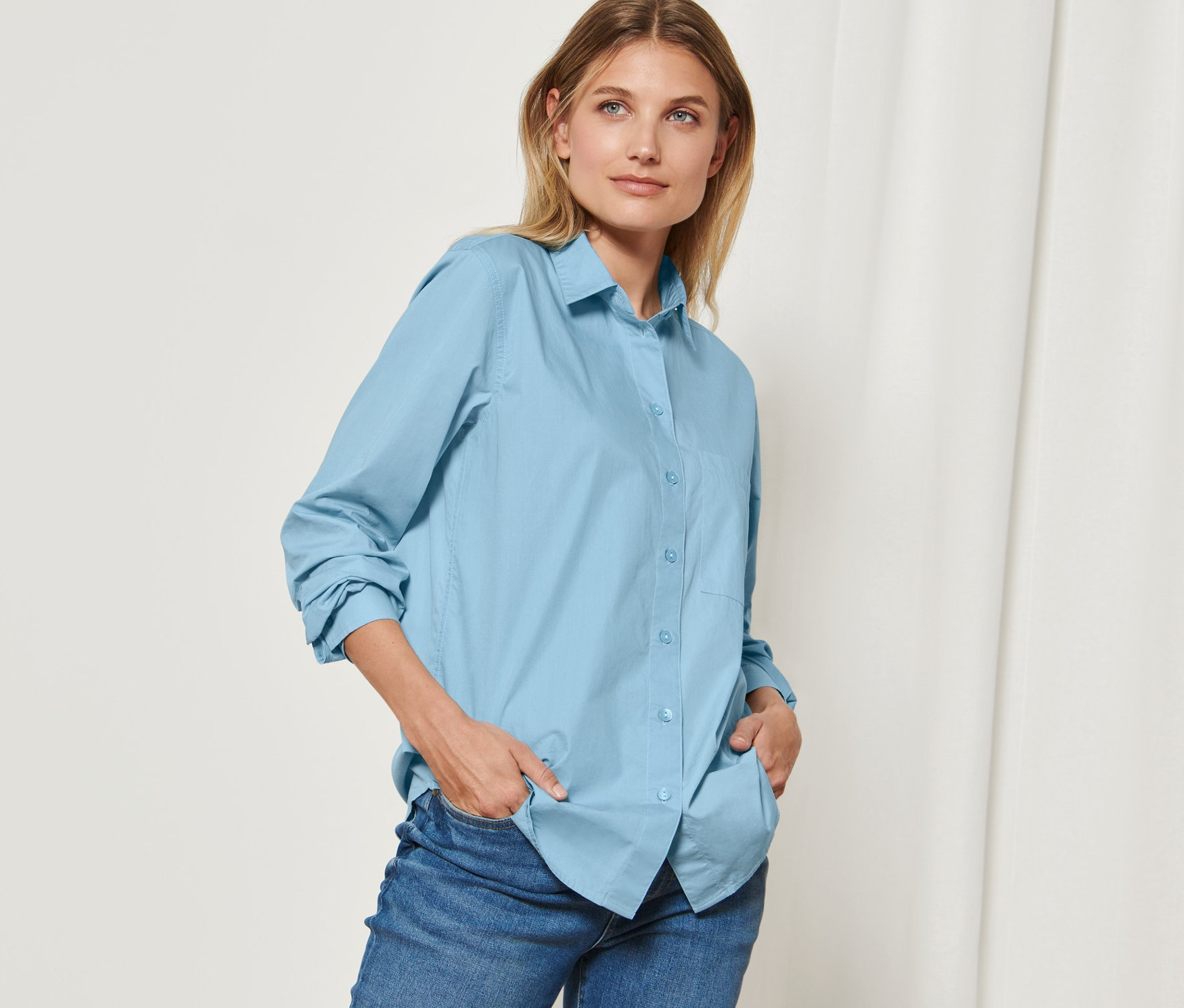 Frau posiert in hellblauer Hemdbluse.