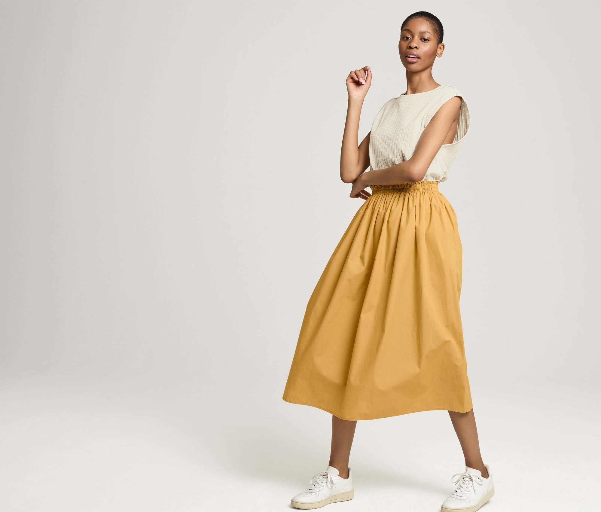 Junge Frau posiert in geringeltem NAH/STUDIO Shirt aus Baumwoll-Hanf-Mix und NAH/STUDIO Rock aus Bio-Baumwolle.