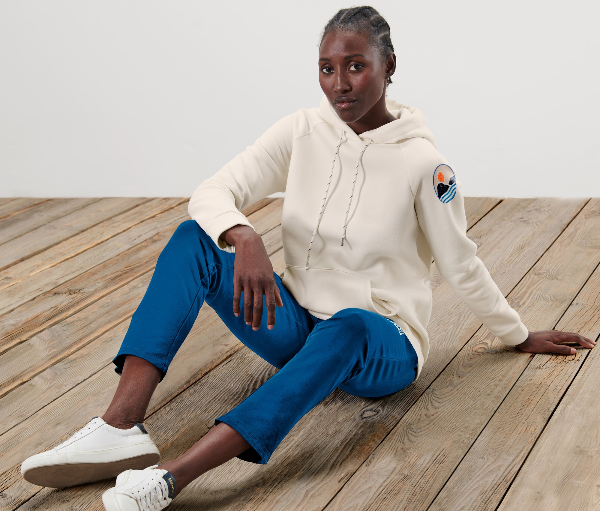 Frau sitzt auf Holzboden und trägt ein beiges Kapuzensweatshirt.