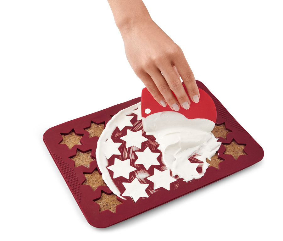 Eine Hand verteilt Zuckerguss auf einer Zimtstern Backmatte.