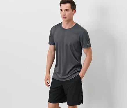 Mann steht mit Händen in den Taschen seiner schwarzen Shorts, er trägt ein graues Funktionsshirt.