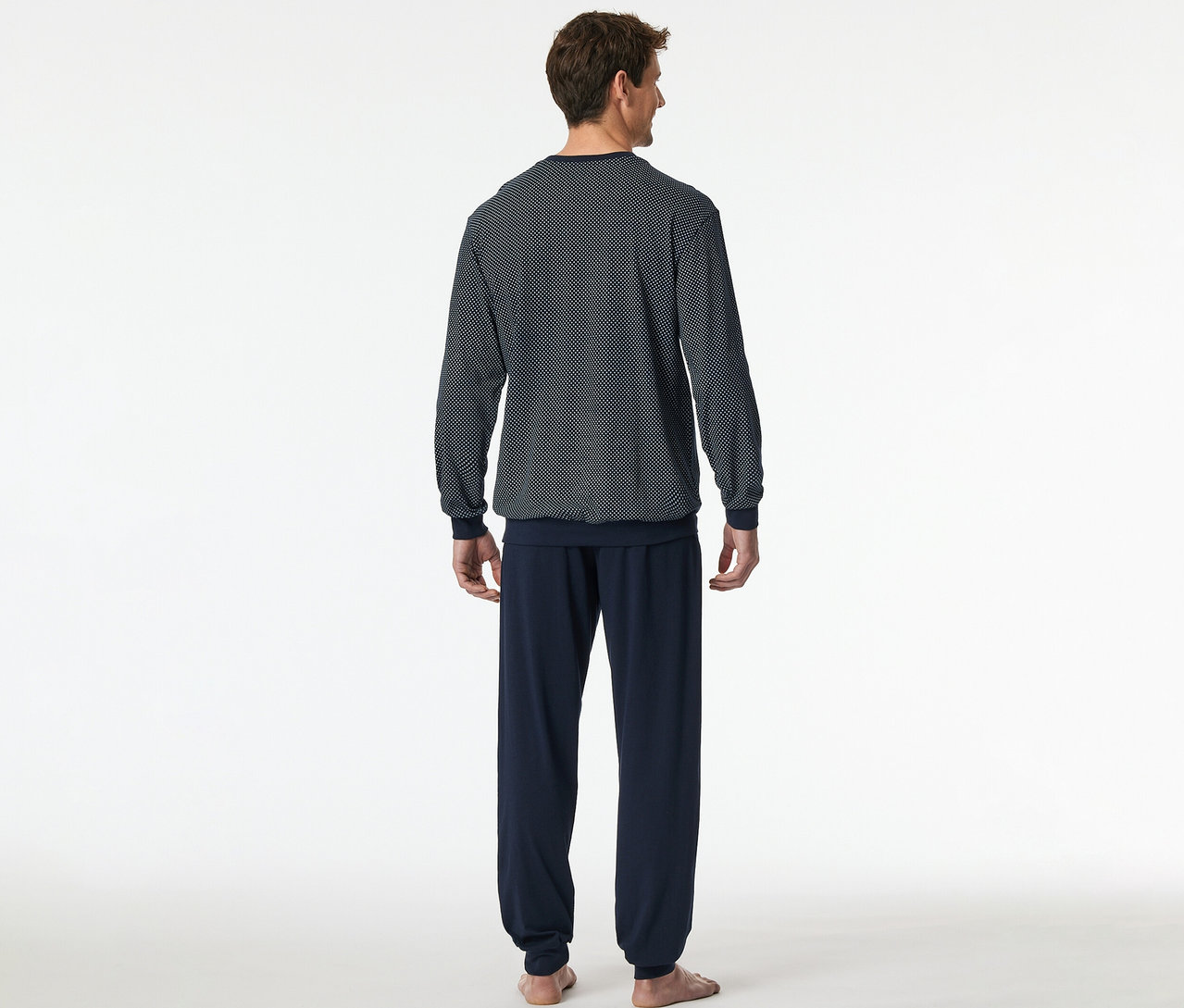 Mann von hinten in einem SCHIESSER Pyjama-Set, bestehend aus einem dunkelblauen Oberteil mit Muster und einer dunkelblauen Hose.