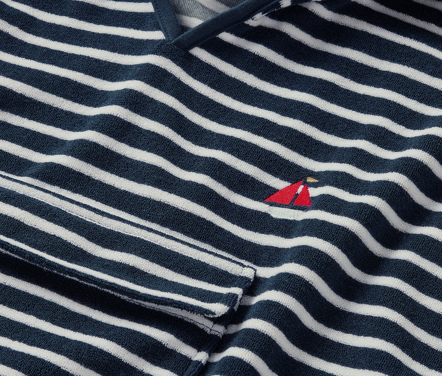 Detailansicht eines Frottierponchos, seaside, mit blau-weißen Streifen und einer kleinen roten Segelboot-Stickerei.