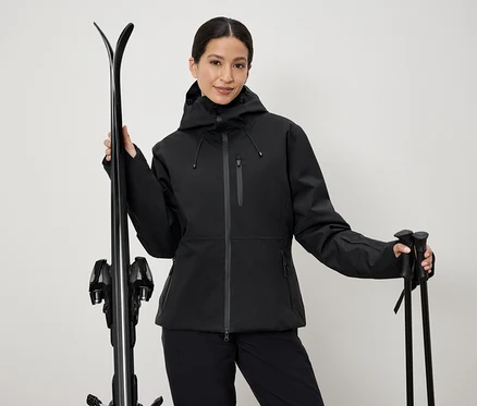 Frau in schwarzer Skijacke hält Ski und Stöcke.