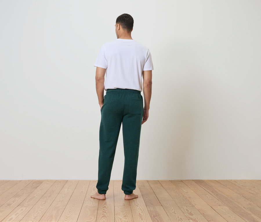Mann mit dem Rücken zur Kamera trägt ein weißes T-Shirt und eine grüne Jogginghose.