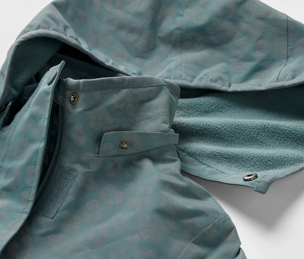 Detail einer Kinder-Thermo-Regenjacke mit reflektierenden Elementen. Die Jacke hat eine Kapuze und einen Reißverschluss.