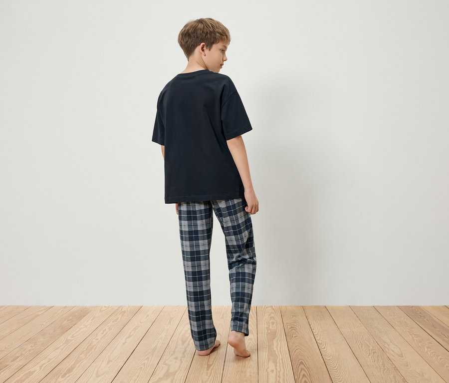 Junge steht mit dem Rücken zum Betrachter, trägt ein schwarzes T-Shirt und eine karierte Schlafanzughose.