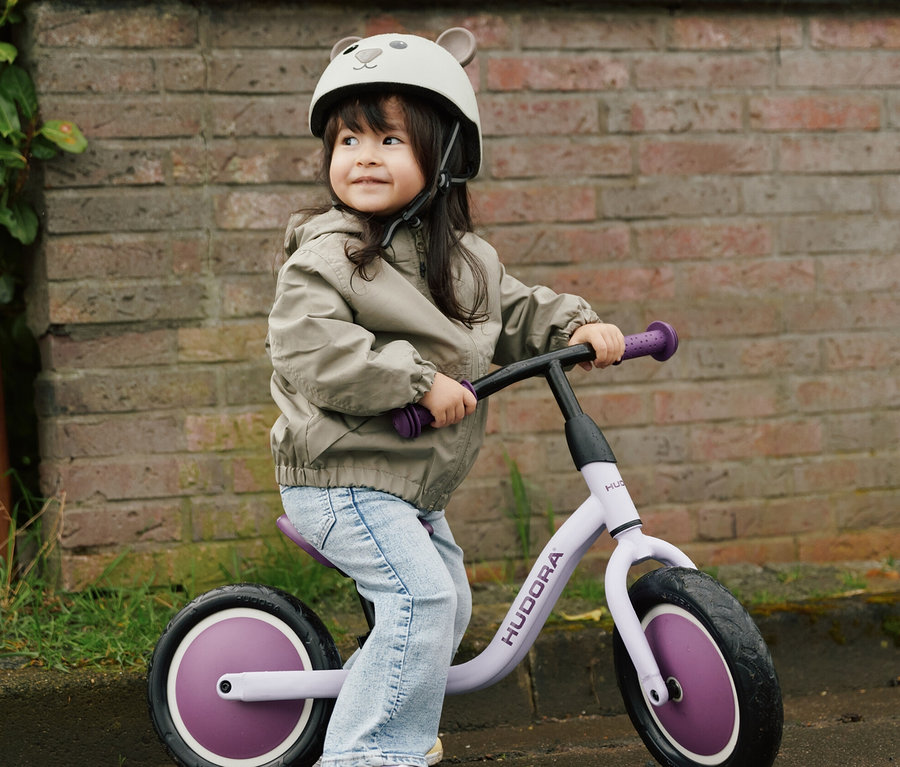 Mädchen auf Laufrad trägt HUDORA Kinderhelm, Beary, 44–47 cm.