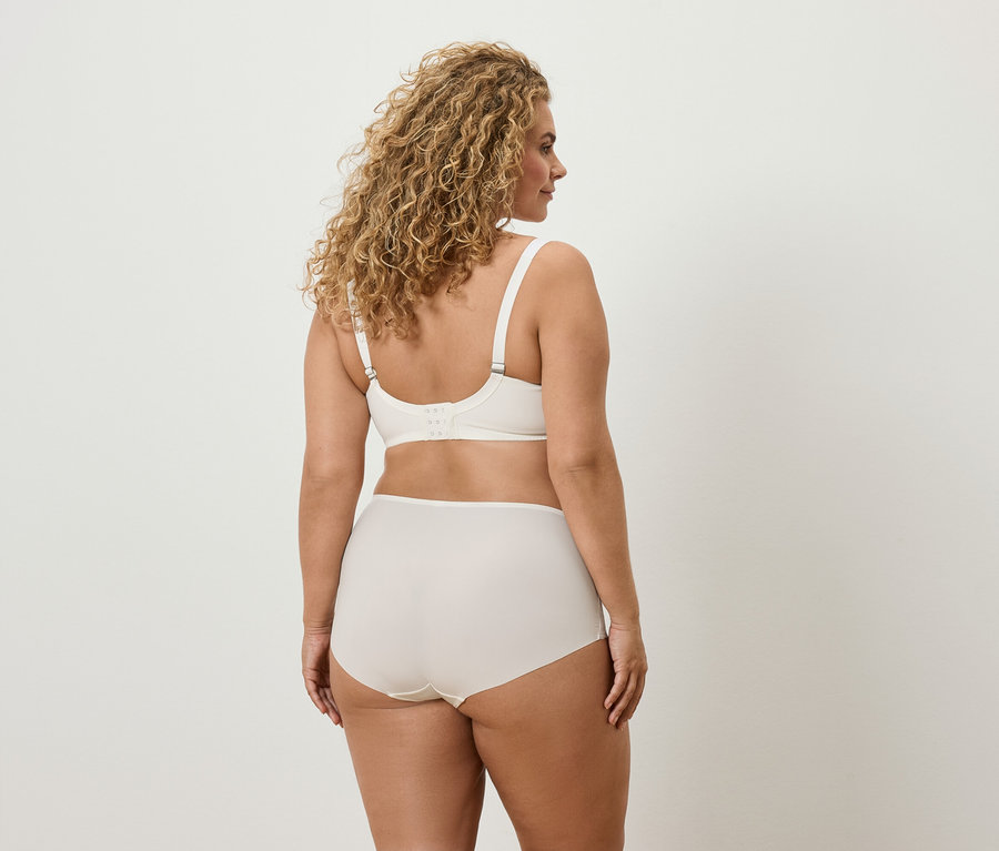 Rückansicht einer Frau mit lockigem Haar, die einen cremefarbenen BH und Slips trägt.