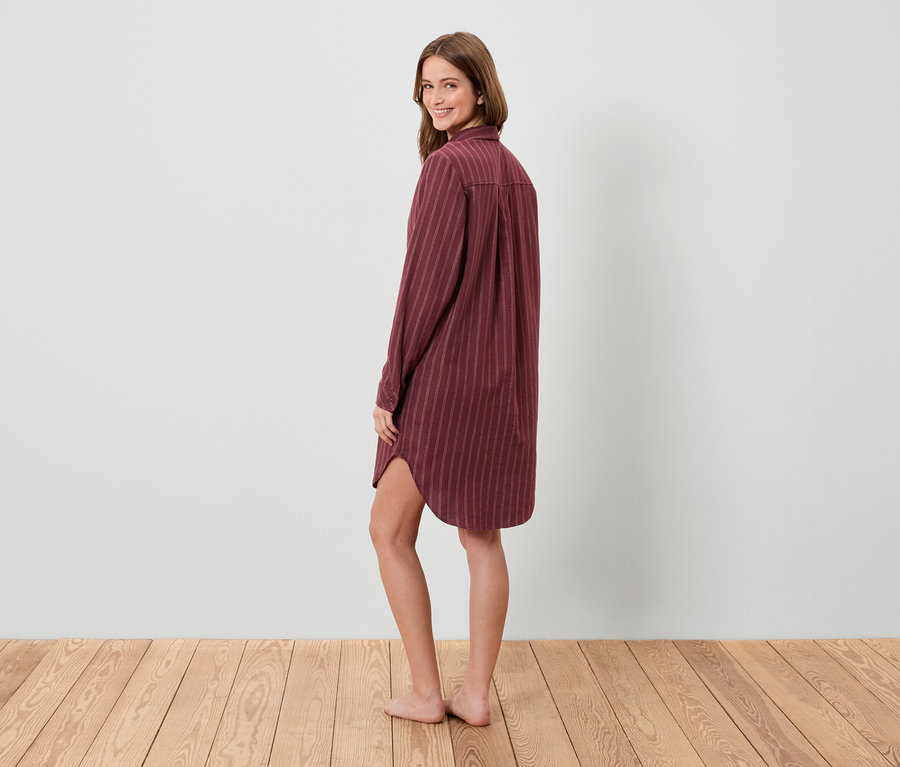 Frau blickt über die Schulter und posiert in einem gestreiften Hemd-Nachthemd.