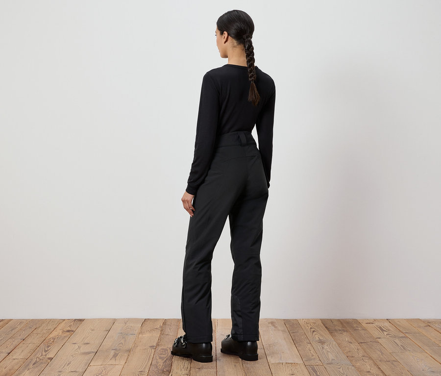 Frau mit schwarzem Pullover und Hose steht mit dem Rücken zur Kamera.