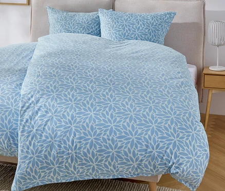 Bett mit blauem Bettbezug mit Blumenmuster und zwei Kissen.