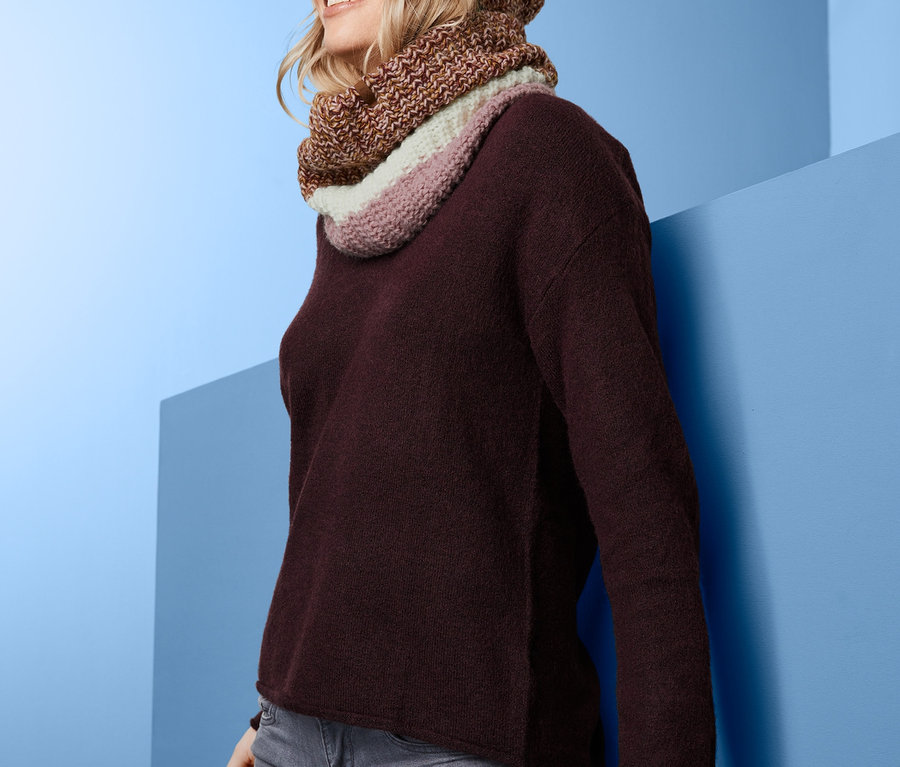 Lächelnde Frau trägt einen Strickschlauchschal und eine Bommelmütze.