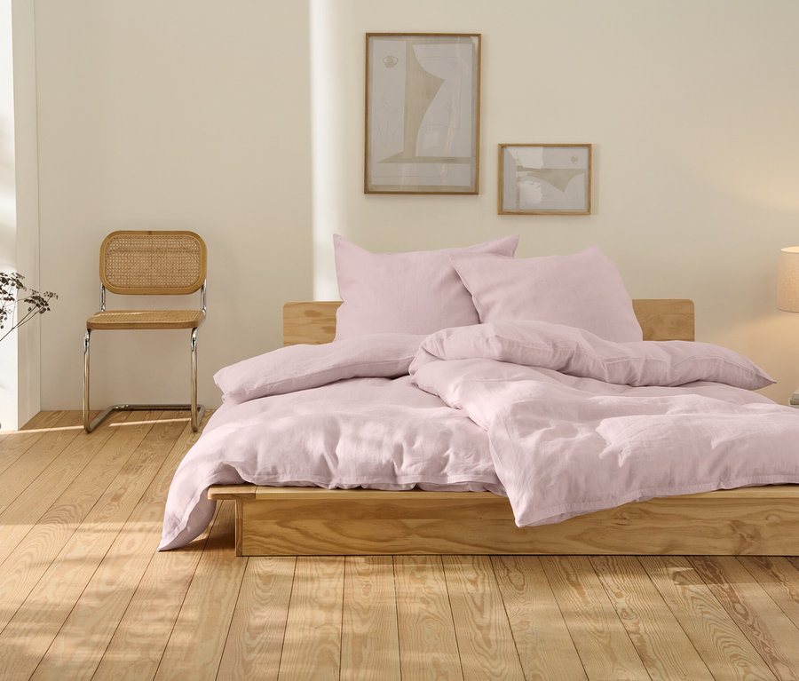 Rosafarbene Leinen-Bettwäsche in Übergröße liegt auf einem Holzbett.