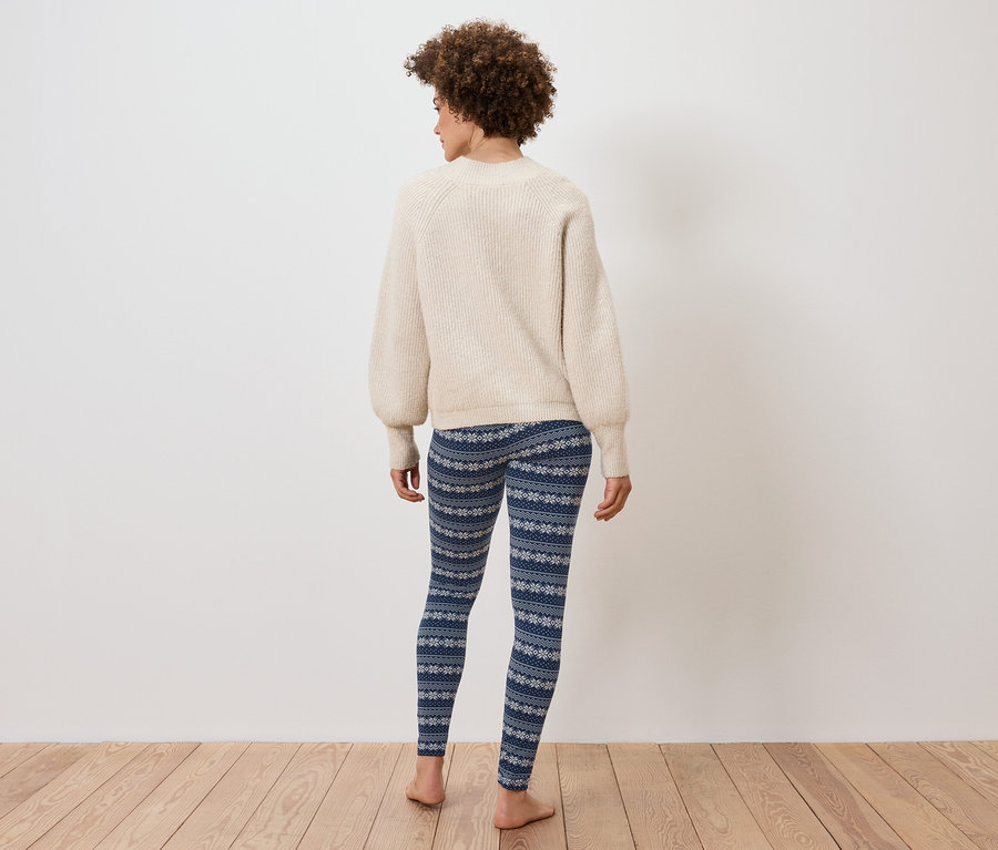 Rückansicht einer Frau mit Afro-Haar, die einen cremefarbenen Pullover und blaue Leggings mit Schneeflockenmuster trägt.