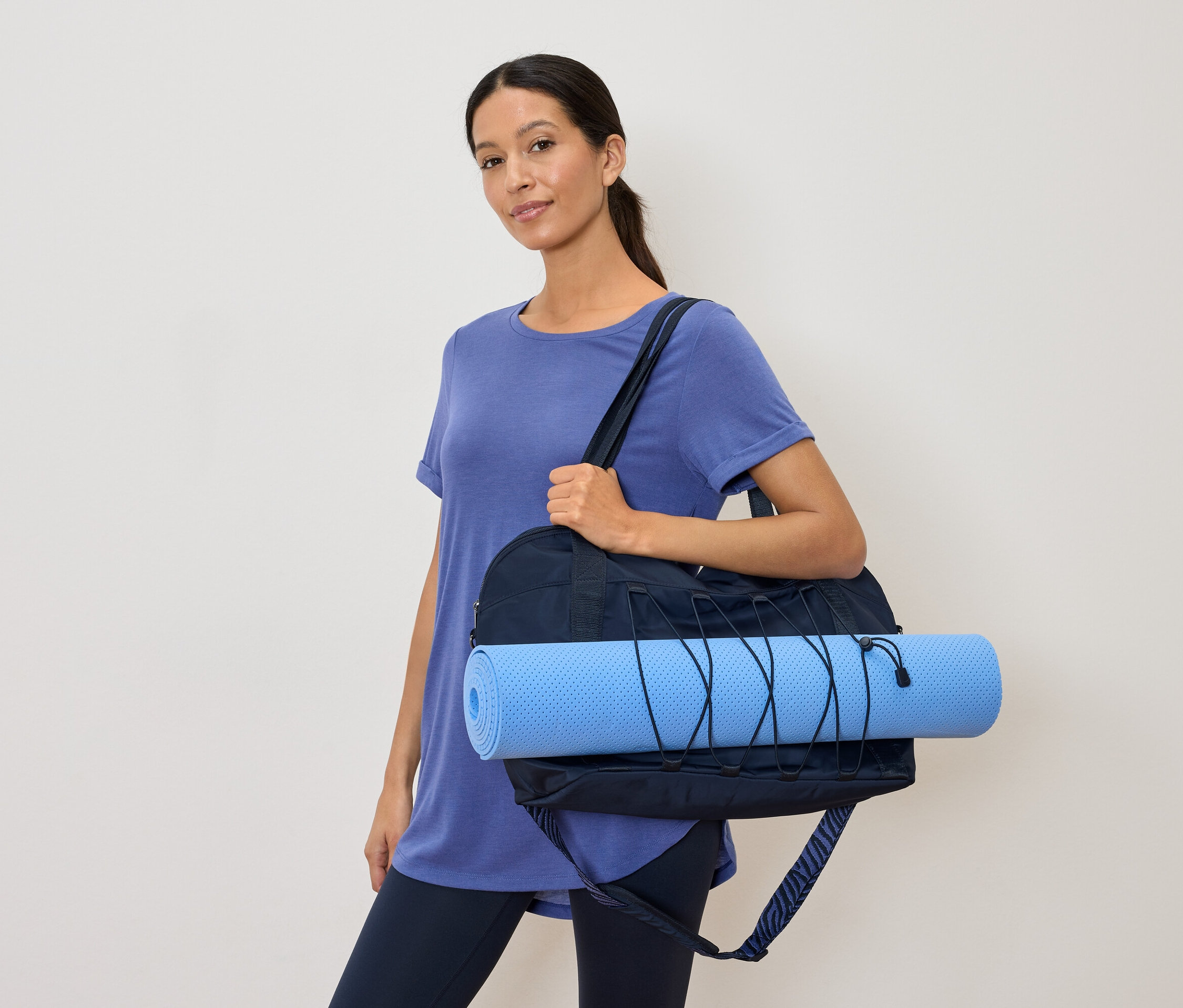 Frau mit marineblauer Sporttasche und hellblauer Yogamatte