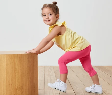 Mädchen schiebt zylinderförmigen Holztisch, trägt pinke 3/4-Leggings.