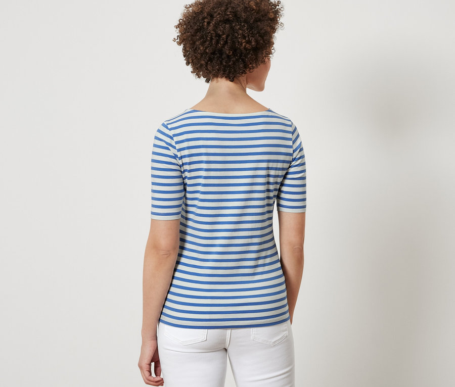 Rückansicht einer Frau mit braunem lockigem Haar, die ein blau gestreiftes Halbarmshirt und weiße Jeans trägt.