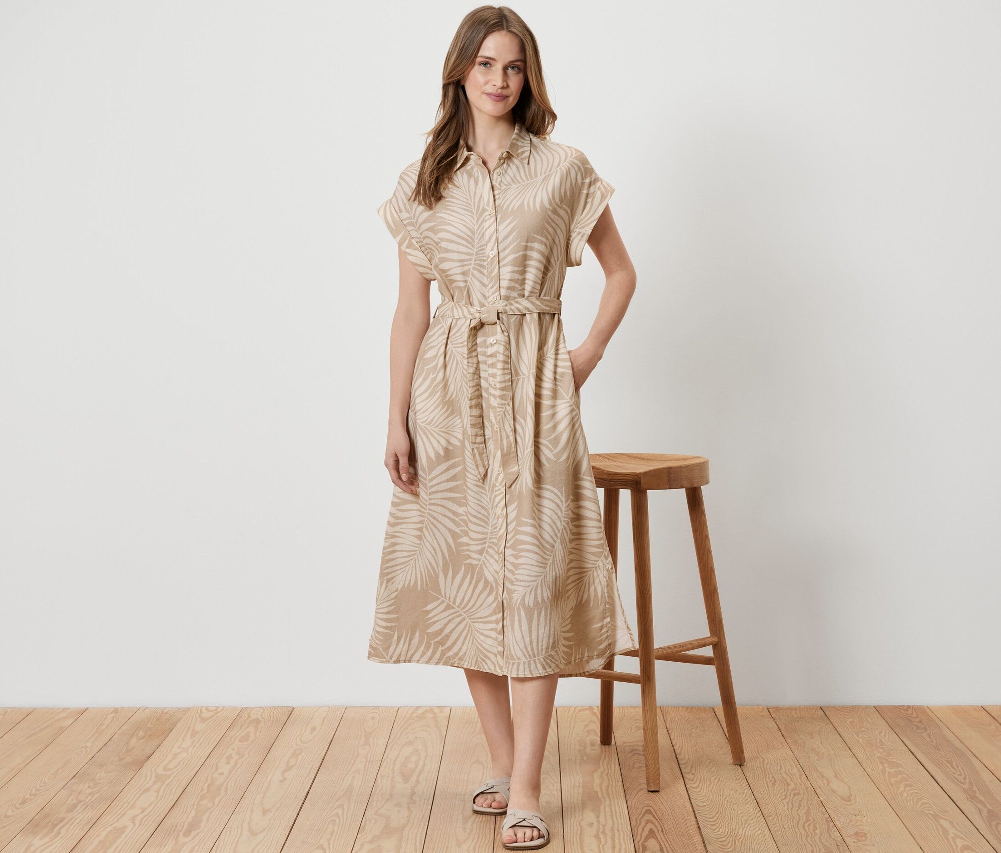 Frau steht neben einem Holzhocker und trägt ein bedrucktes Leinenkleid.