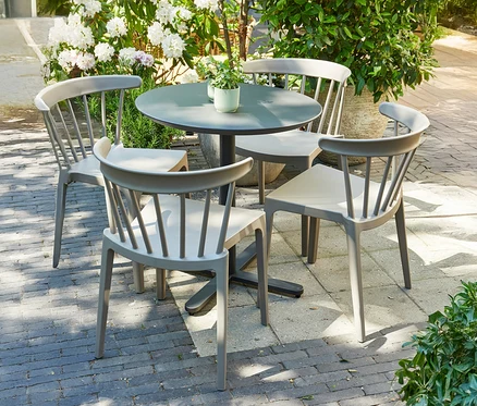 Grauer Gartentisch mit vier Stühlen auf einer Terrasse, umgeben von Pflanzen.